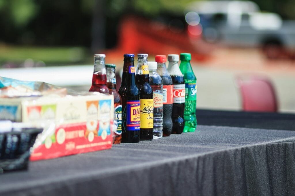 Assorted bottles of soft drinks on a table outdoors during the day.