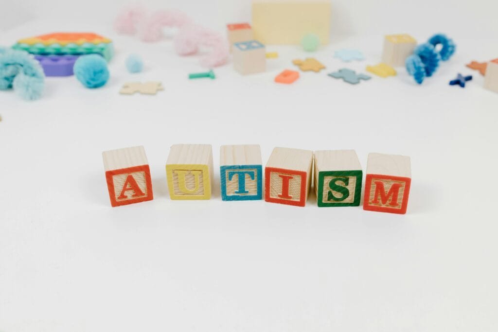 Wooden blocks spelling autism surrounded by colorful toys on a white background.