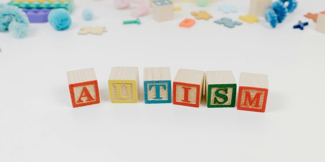 Wooden blocks spelling autism surrounded by colorful toys on a white background.