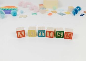 Wooden blocks spelling autism surrounded by colorful toys on a white background.
