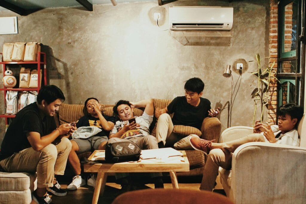 Five young men relaxing indoors, chatting and using phones in a Jakarta café.