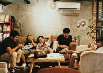 Five young men relaxing indoors, chatting and using phones in a Jakarta café.