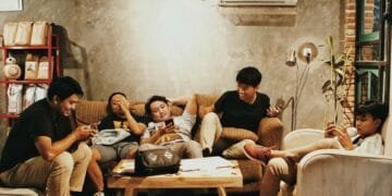 Five young men relaxing indoors, chatting and using phones in a Jakarta café.