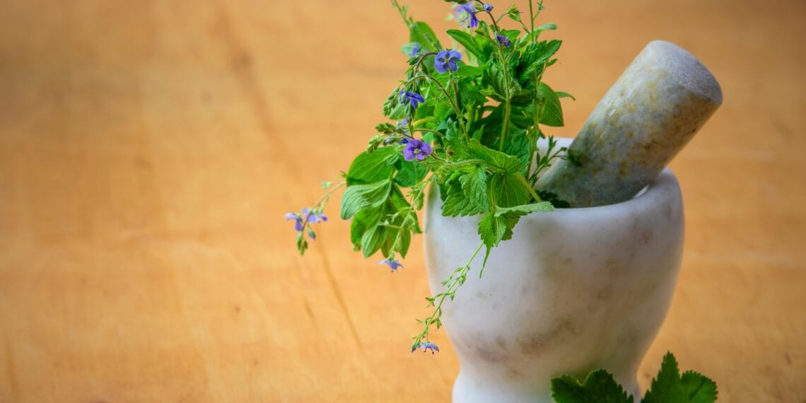 Marble mortar and pestle with fresh herbs and flowers on wooden table enhancing natural health and cooking aesthetics.