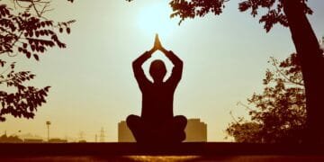 Silhouette of a person practicing yoga outdoors during sunrise, creating a calming atmosphere.
