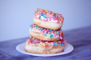 A stack of doughnuts covered in colorful fruity pebbles on a plate.