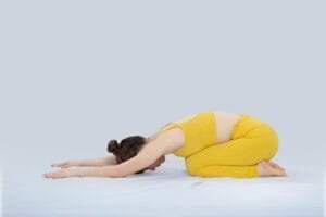 A woman in yellow sportswear performing a yoga child's pose on a white background.