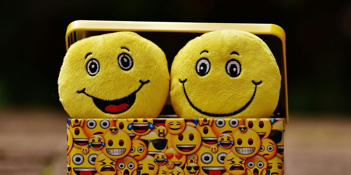 Two yellow smiley plush toys in an emoji-themed box, expressing fun and happiness.