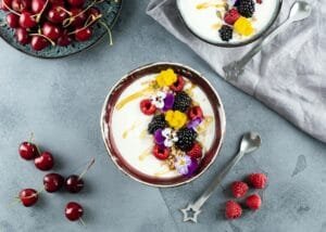 Flat lay of a vibrant yogurt bowl topped with blackberries, raspberries, and cherries, shot from above.