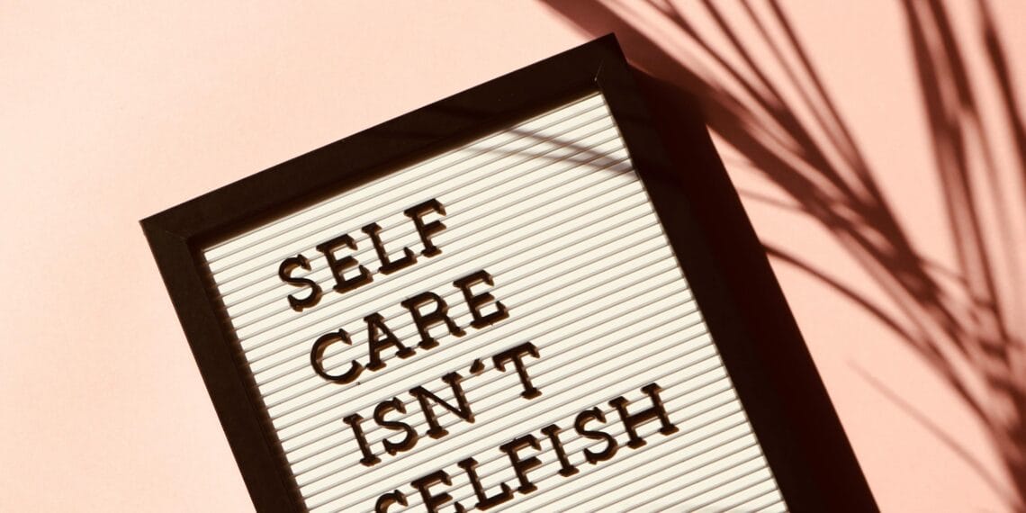 Letter board displaying 'Self Care Isn't Selfish' with artistic shadow on pink background.