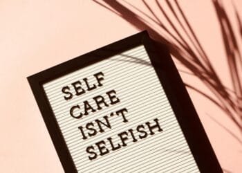 Letter board displaying 'Self Care Isn't Selfish' with artistic shadow on pink background.