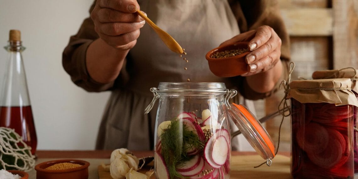 Hands preparing pickled vegetables in a jar, capturing a rustic and organic lifestyle.