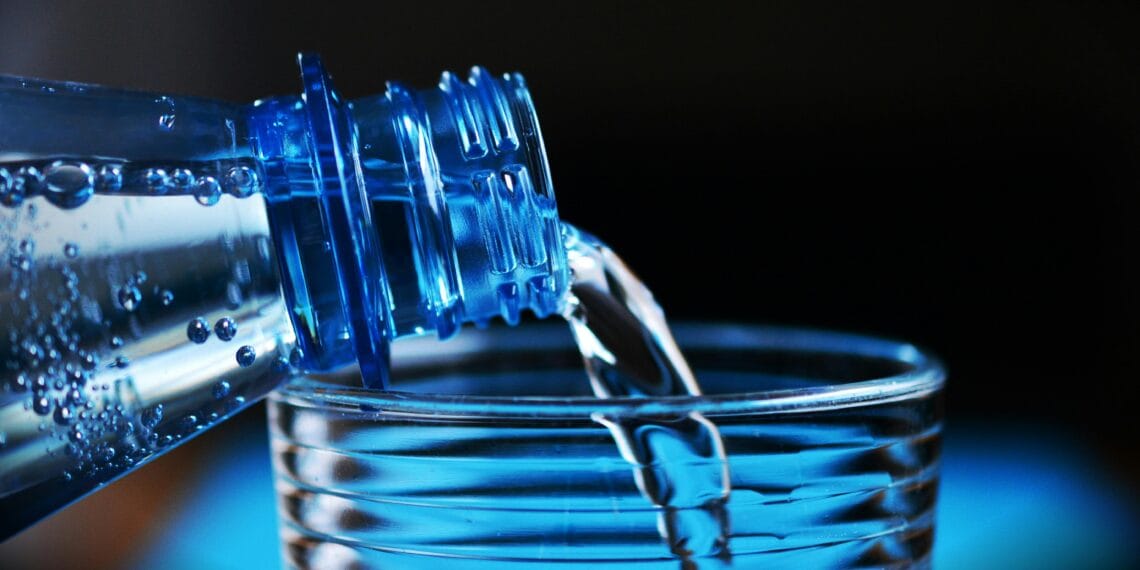 Close-up of sparkling water being poured from a bottle into a glass with bubbles visible.