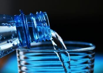 Close-up of sparkling water being poured from a bottle into a glass with bubbles visible.