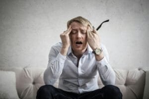 Stressed man sitting on couch, feeling overwhelmed and frustrated, expressing mental strain.