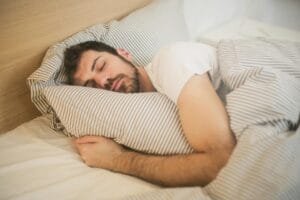 Man sleeping peacefully on striped bedding, embracing relaxation and comfort.