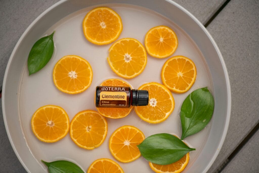 Clementine essential oil bottle with fresh orange slices and green leaves in a round dish.