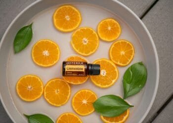 Clementine essential oil bottle with fresh orange slices and green leaves in a round dish.
