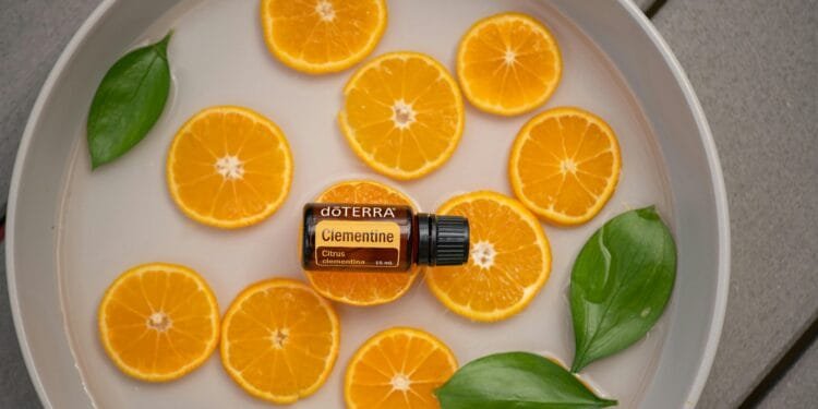 Clementine essential oil bottle with fresh orange slices and green leaves in a round dish.