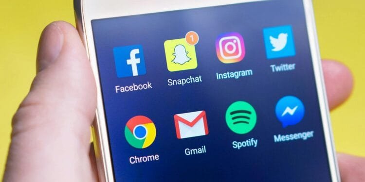 A person's hand holding a smartphone displaying social media and communication apps.