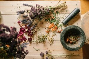 Flat lay of dried herbs and flowers with a stone mortar and pestle on a rustic wooden table.