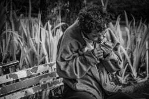 Black and white photo of an elderly man lighting a cigarette on a park bench.