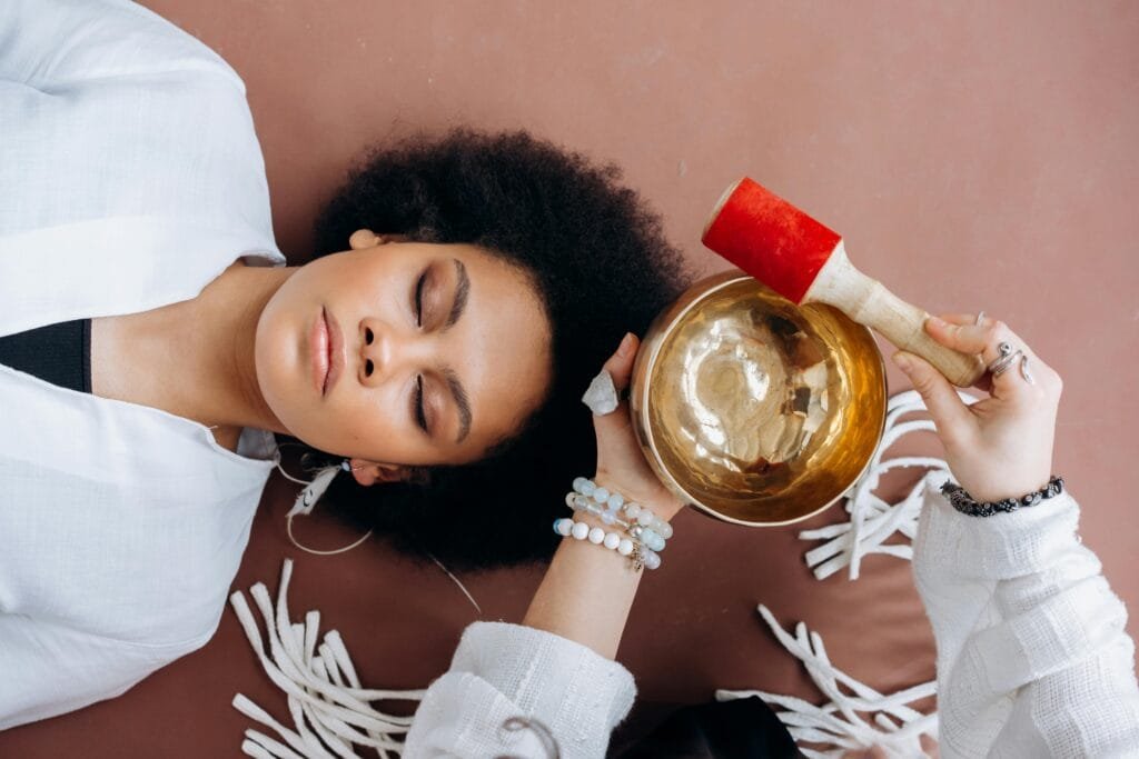 A woman experiencing sound healing therapy with a Tibetan singing bowl indoors