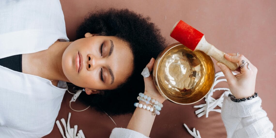 A woman experiencing sound healing therapy with a Tibetan singing bowl indoors