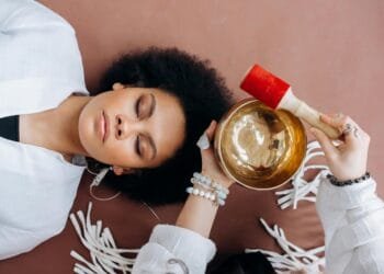 A woman experiencing sound healing therapy with a Tibetan singing bowl indoors