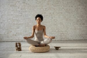 Woman practicing yoga meditation on cushion indoors, embracing peace and wellness.