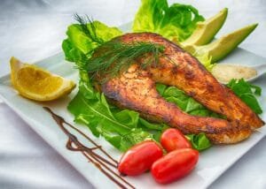 Delicious grilled salmon served with fresh vegetables and herbs on a white plate.