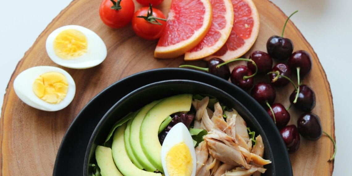 A vibrant, healthy salad bowl with avocado, eggs, tomatoes, grapefruit, and cherries on a wooden board.
