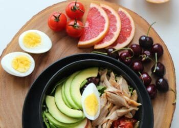 A vibrant, healthy salad bowl with avocado, eggs, tomatoes, grapefruit, and cherries on a wooden board.