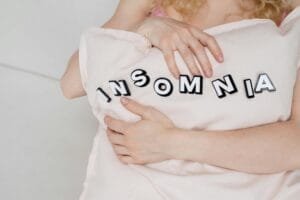 Close-up of a woman holding a pillow with 'insomnia' text, depicting sleep disorder.