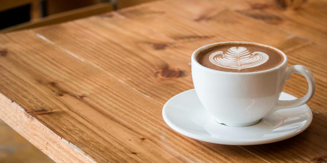 Close-up of a white cup of latte with artistic foam on a rustic wooden table.
