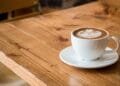Close-up of a white cup of latte with artistic foam on a rustic wooden table.