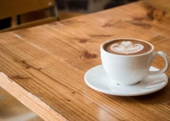 Close-up of a white cup of latte with artistic foam on a rustic wooden table.