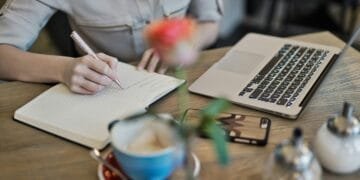 Woman writing in a notebook with a laptop and coffee cup on a desk. Ideal for workspace inspiration.