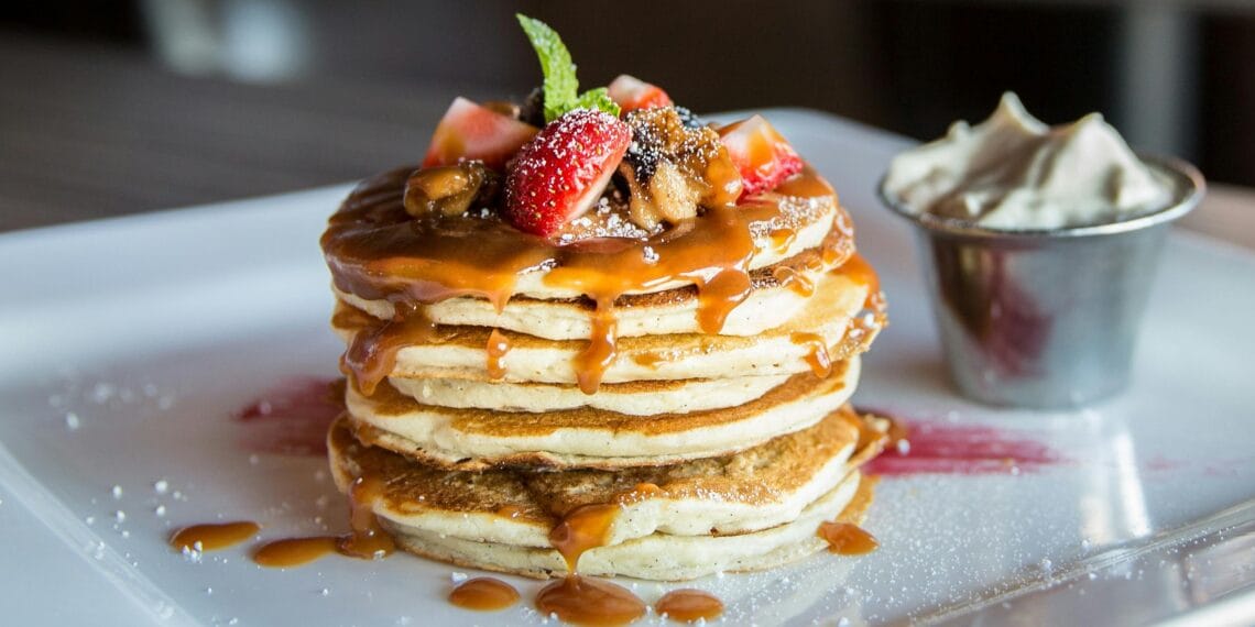 Mouthwatering pancakes with strawberries, nuts, and syrup on a plate.