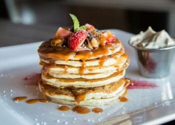 Mouthwatering pancakes with strawberries, nuts, and syrup on a plate.