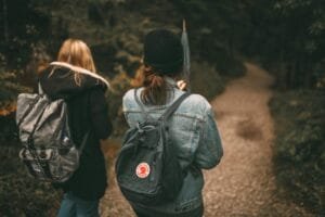 Two friends explore a forest trail together with backpacks, enjoying nature.