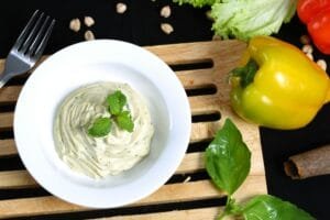 A fresh herb dip paired with vibrant bell peppers on a wooden surface, perfect for healthy snacking.