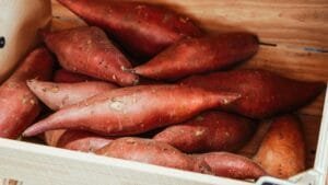 Close-up of fresh sweet potatoes in a wooden crate, ideal for cooking.