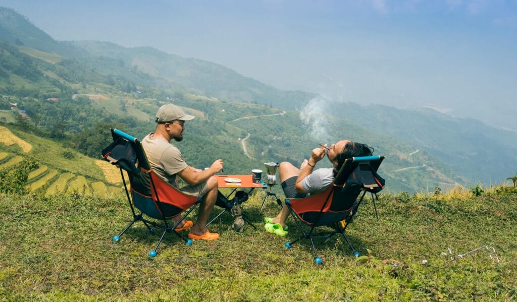 Two men relaxing with cigarettes and coffee, overlooking stunning mountain landscapes. Perfect for adventure themes.