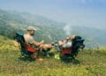 Two men relaxing with cigarettes and coffee, overlooking stunning mountain landscapes. Perfect for adventure themes.