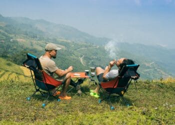 Two men relaxing with cigarettes and coffee, overlooking stunning mountain landscapes. Perfect for adventure themes.