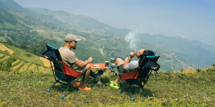 Two men relaxing with cigarettes and coffee, overlooking stunning mountain landscapes. Perfect for adventure themes.