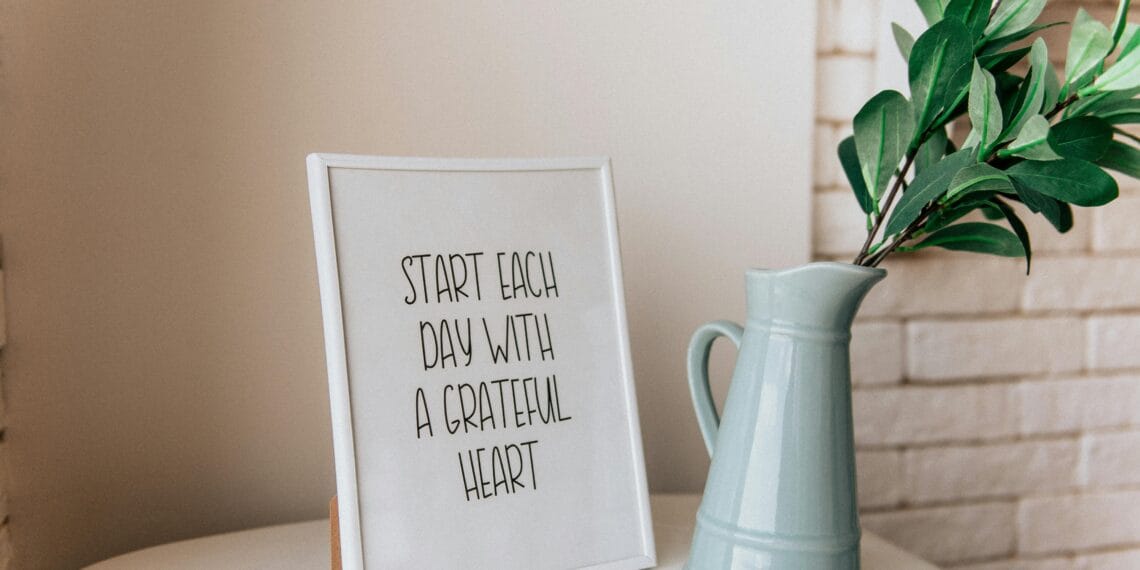 Framed quote 'Start each day with a grateful heart' next to a vase indoors.