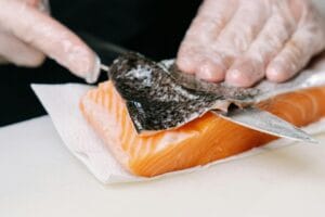 Close-up of salmon skin being removed by hands with a knife, showcasing food preparation.