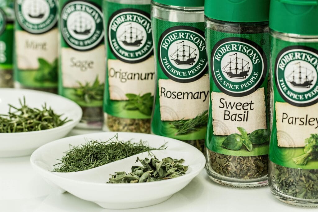 Assorted dried herbs in branded spice jars with bowls of loose herbs in the foreground.